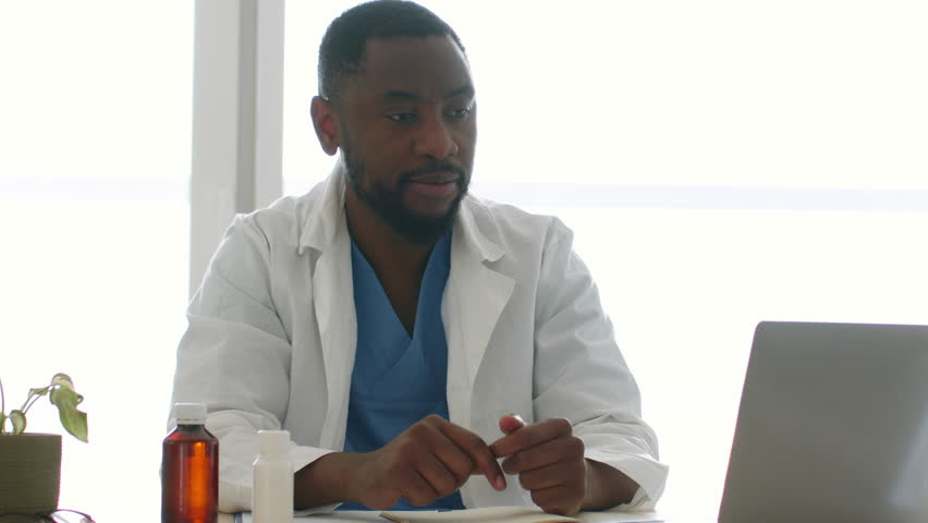 Young professional african american therapist video chatting with patient online on laptop, recommending new pills, sitting in office, tracking shot, slow motion, free space Royalty-Free Stock Footage #1098528673