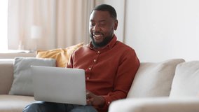 Great streaming service. Young happy african american man watching digital tv on laptop and laughing, enjoying favorite show online at home, tracking shot, slow motion, empty space