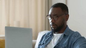 Overwork concept. Young focused african american guy working on laptop, feeling tired, taking off his eyeglasses and rubbing his nose bridge, tracking shot, slow motion