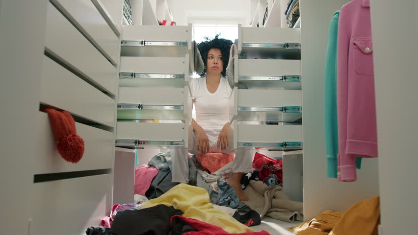 Spring cleaning and clearance concept. Upset desperate woman of color with curly black hair angrily closing drawers with clothes. African American woman in messy bedroom organizing cloths at wardrobe Royalty-Free Stock Footage #1098531017