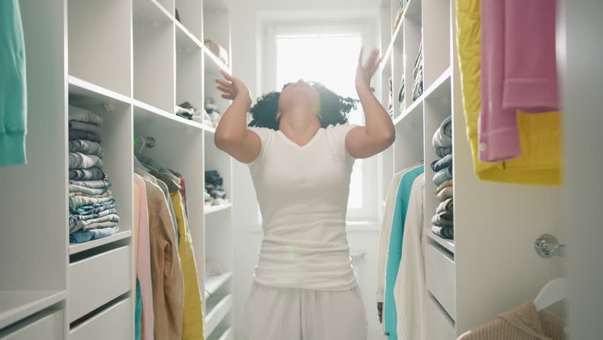 I do not know what to wear, Help me, head on hands. Desperate African American woman wrapped head in hands looking on racks full colorful clothes thinking what to wear, trying make difficult decision | Shutterstock HD Video #1098531019