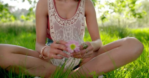 Smiling boho girl wearing vintage lace headband holding a pink daisy flower in a summer park, Panning in Slow Motion