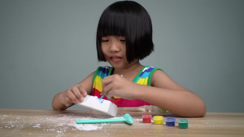 Chinese girl with rainbow color dress dig the hole of gypsum and search for treasure. Child hobby, creativity concept