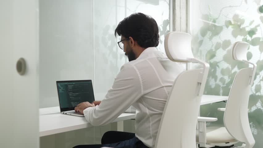 Portrait of handsome happy professional Indian programmer coding on laptop looking at camera smiling. Beautiful qualified male IT worker developing apps doing tasks in bright office. | Shutterstock HD Video #1098542839