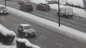 The video appears to show cars driving quickly through the snow on a two-way road in a city. The cars are leaving trails of snow behind them as they move. It is not clear where this scene is taking pl