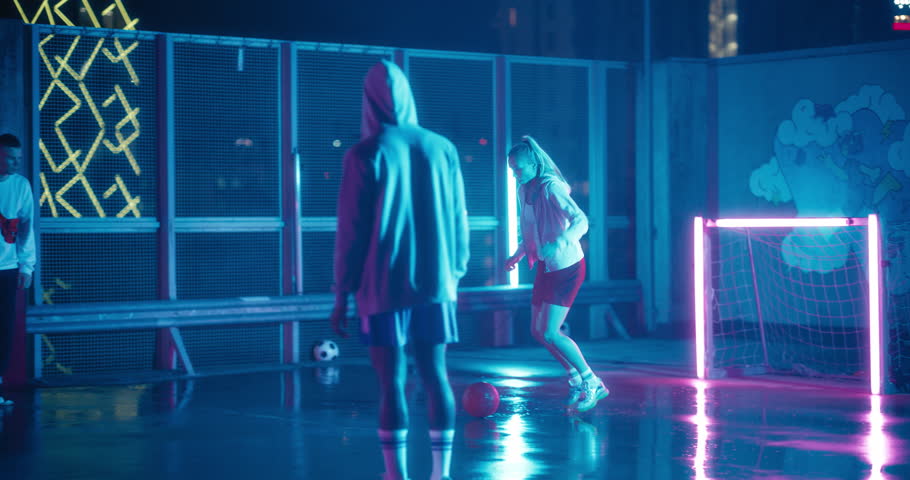 Empowering Sporty Young Woman Playing Soccer with Friends, Dribbling, Scoring a Successful Goal. Female Footballer Playing Football Outside at Night on Rooftop Urban City Spot with Neon Lights