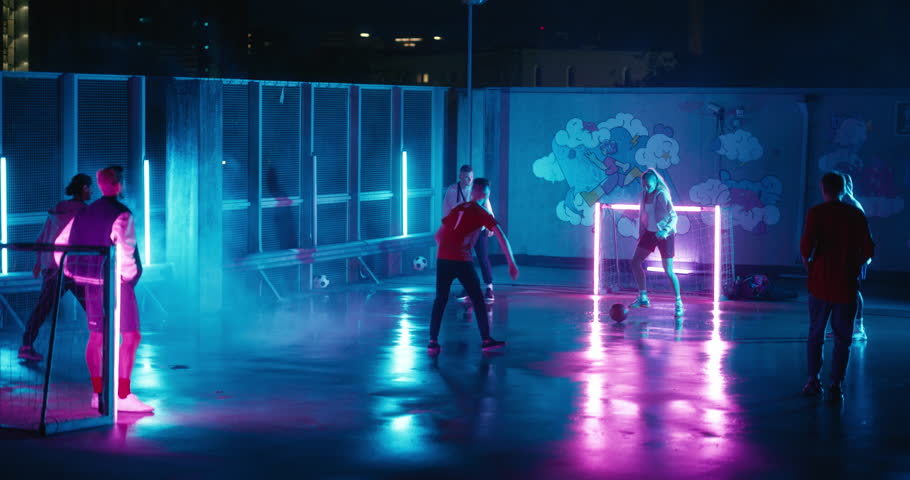 Young Female Playing Soccer with Diverse Group of Friends, Dribbling, Scoring a Successful Goal. Female Footballer Playing Football Outside at Night on Rooftop Urban City Spot with Neon Lights