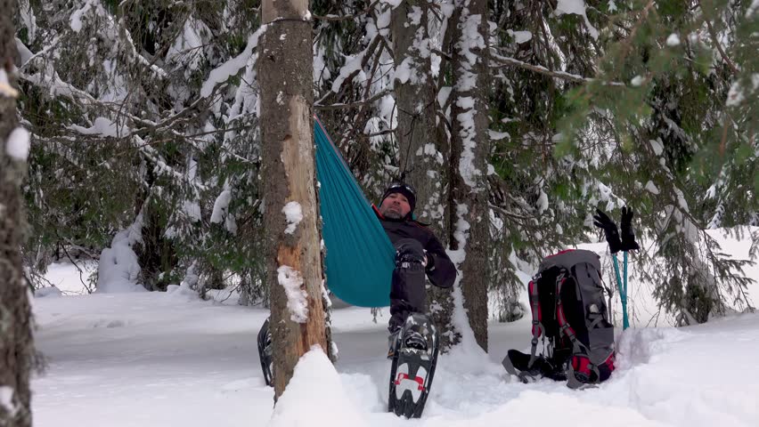 Hiker with snowshoes lying in hammock under the trees in the winter forest. Man relaxing. Camping in winter Royalty-Free Stock Footage #1098546709