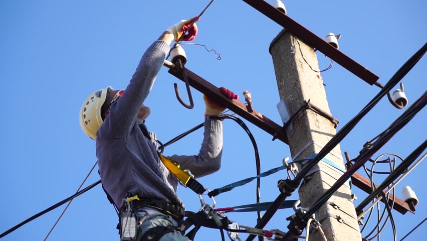 Skilled electrician in helmet fixes wires standing on ladder near high pole against blue sky on summer day backside view. Electrical service and mounting on the pole. Slow motion Royalty-Free Stock Footage #1098550665