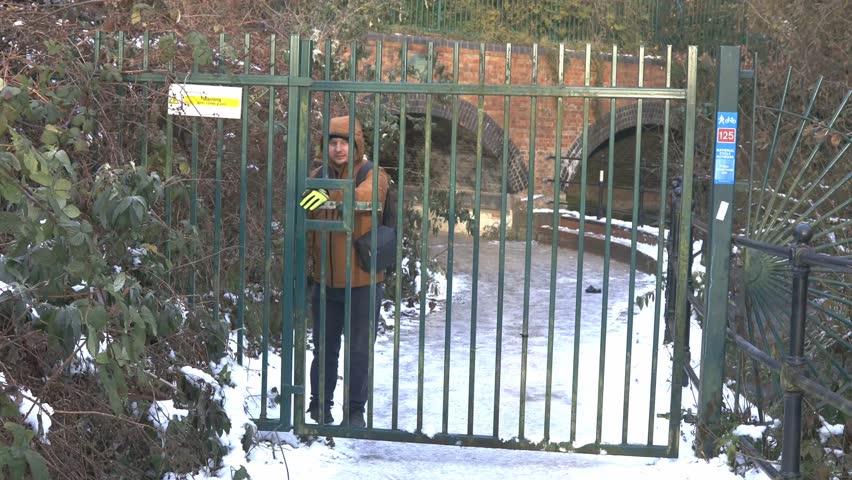 caucasian male wearing orange jacket open a iron gate welcoming visitor in white snow landscape park forest