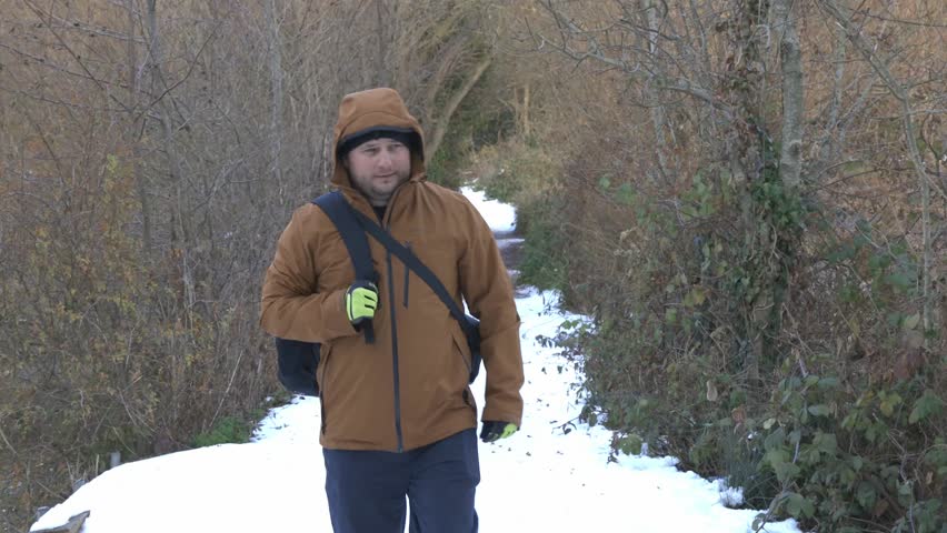 caucasina male wearing orange jacket walking alone in the forest with white snow winter landscape