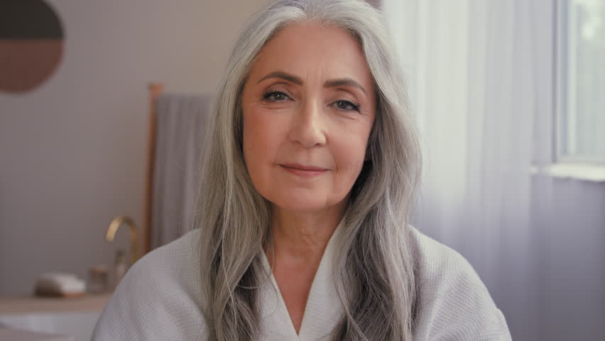 Portrait indoors old Caucasian 50s senior model gray-haired mature woman 60s lady in bathroom showing jar of anti-aging cosmetic natural organic sunscreen mineral cream moisturizing face skin care Royalty-Free Stock Footage #1098559531