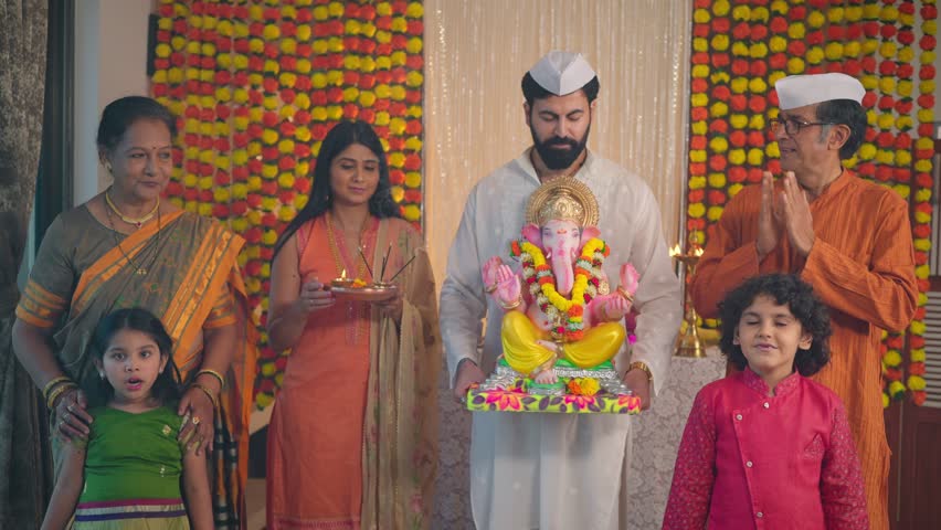 Happy ethnic Hindu Indian young man holding a Ganapati idol with smiling family members in traditional clothes looking at the camera during Ganesha Chaturthi festival or celebration in decorated house Royalty-Free Stock Footage #1098559835