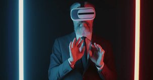 Slow motion of mature businessman wearing VR glasses enjoying new technology moving hands against black background with neon illumination