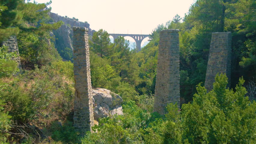 Historical Arches Bridge railway slow zoom-in 4k aerial drone between mountains and a vast green forest on a sunny day and bright sky. Vintage bridge with several arches. An old bridge in Turkey