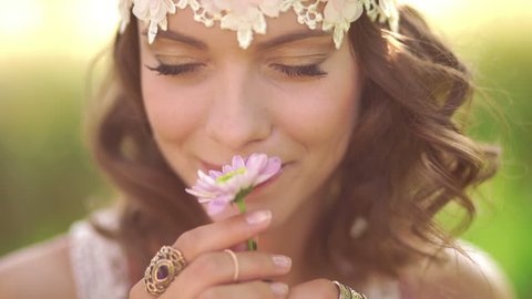 Daydreaming girl in boho fashion with a vintage lace headband smelling a flower while sitting in a sunlit summer park