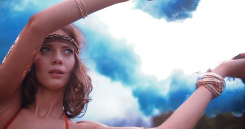 Boho girl turning her arms with blue smoke flares in nature in Slow Motion