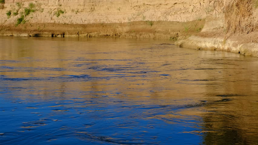 Water surface of the river in the canyon at sunset; golden reflection and magical ripple structure