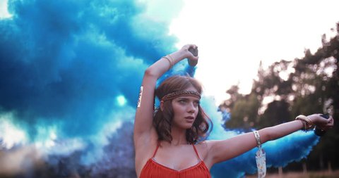 Boho girl turning her arms with blue smoke flares in nature in Slow Motion