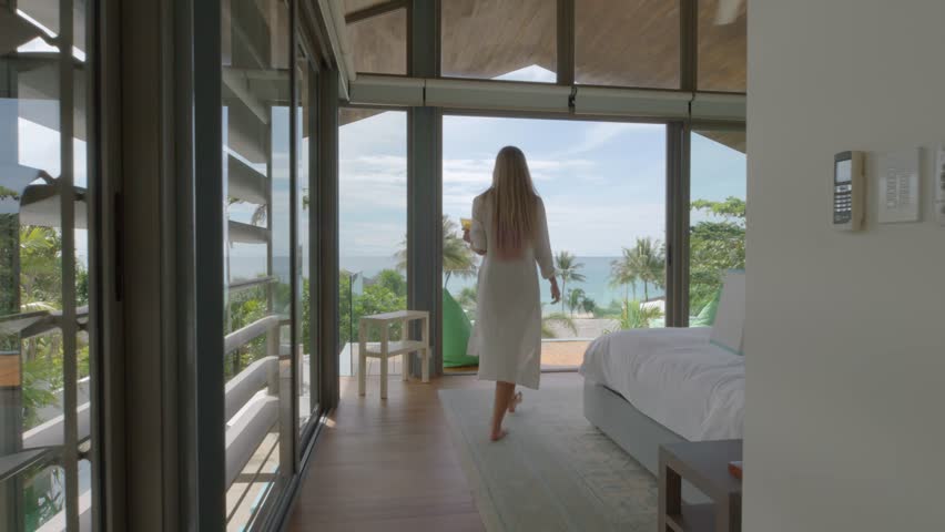 Woman walks through the bedroom with drink in the hand to the balcony with sea view Royalty-Free Stock Footage #1098574263