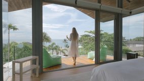 Woman walks through the bedroom with drink in the hand to the balcony with sea view - Powered by Shutterstock - Get 15% off with code: PIKWIZARD15