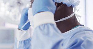 Video of african american male surgeon tying face mask in operating theatre, copy space. Hospital, medical and healthcare services.