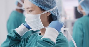 Video of asian female surgeon tying face mask in operating theatre, copy space. Hospital, medical and healthcare services.