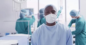 Video portrait of african american male surgeon in mask smiling in operating theatre, copy space. Hospital, medical and healthcare services.