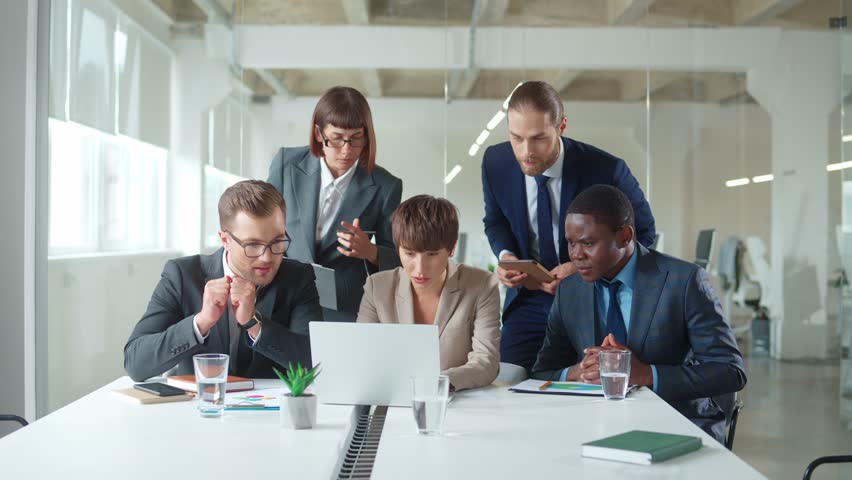 Multi ethnic colleagues gather in modern office boardroom using computer discussing common project, reading good news about company. Teamwork activity. staff members excited about professional win Royalty-Free Stock Footage #1098580671