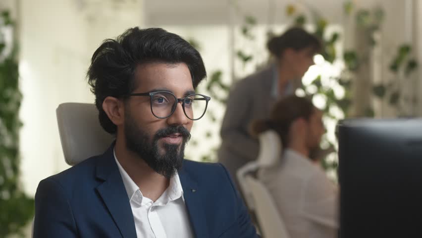 Close-up portrait of focused professional Indian developer coding using computer in modern IT company. Qualified bearded male programmer wearing suit and glasses in office. IT concept. | Shutterstock HD Video #1098580791