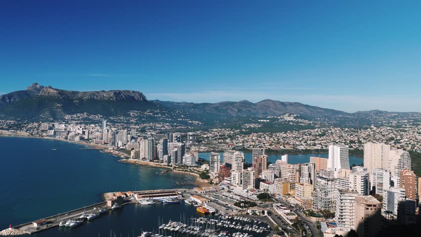 Calpe city landscape, Spain. Coastline of Mediterranean Sea with buildings, hotels and sandy beach at sunny day. Calpe cityscape with beaches and mountains. Popular travel destination. Tourism concept