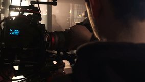 Cameraman adjusts lens of large modern camera at shooting set close backside view slow motion. Movie production