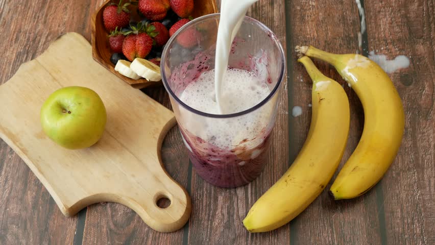 Making Fruit Smoothie with banana, blueberry, apple, strawberry and milk. Blender filled with fresh whole fruits for making a smoothie