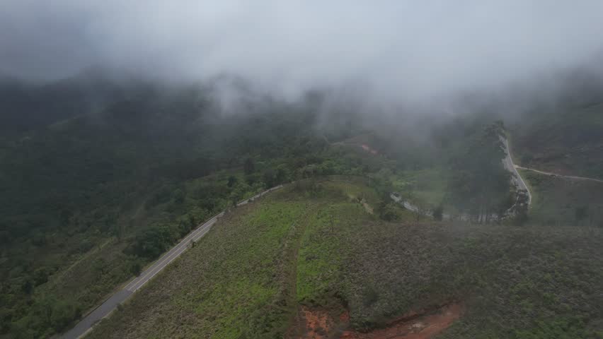 Dense fog covering small hills in a small town. Small houses, dense vegetation and low clouds. Dark scenery, with low lighting.