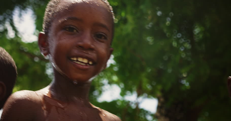 Close Up on a Group of Happy and Innocent Black Children Playing and Enjoying the Blessing of Rain Water After Long Drought. Authentic African Kids Jumping and Laughing when Water Gets Poured on Them. Royalty-Free Stock Footage #1098588531
