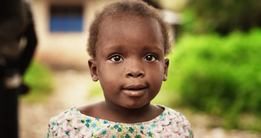 Close Up Portrait of a Cute African Little Todller Looking at the Camera with Blurred People Moving in the Background. Black Child Full of Innocence and Joy, Representing Hope for a Better Future Royalty-Free Stock Footage #1098588563