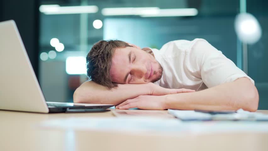 Young overworked employee sleeping at office desk at workplace with laptop startup finance job. Lazy entrepreneur exhausted and sleepy due to work stress. Defeated by the deadline. Нard work | Shutterstock HD Video #1098590977