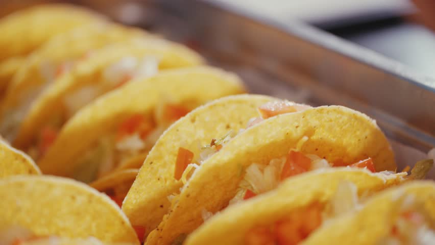 A closeup shot of tongs picking up tacos and putting them on a cafeteria tray