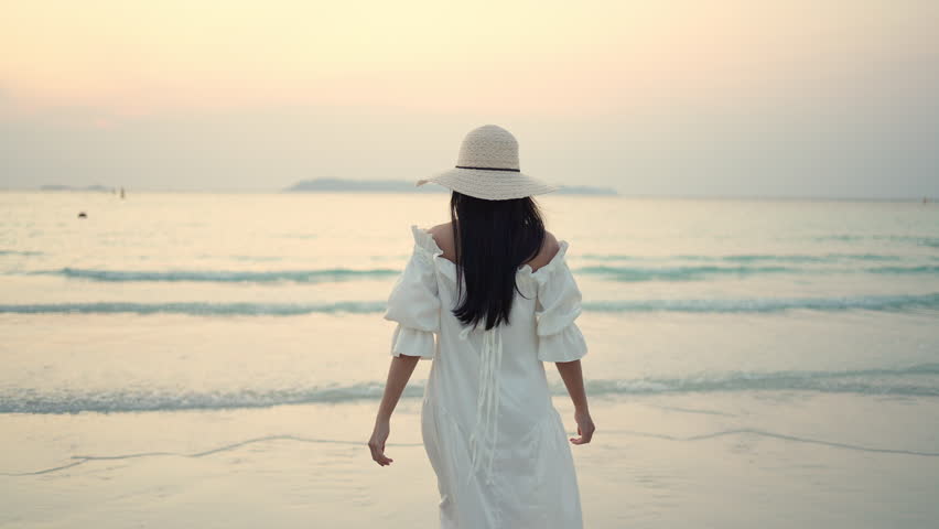 Young Asian woman in white dress walking on the beach while travel tropical island on summer holiday vacation vacation at sunset. Attractive girl relax and enjoy outdoor lifestyle walking at seaside. | Shutterstock HD Video #1098593057