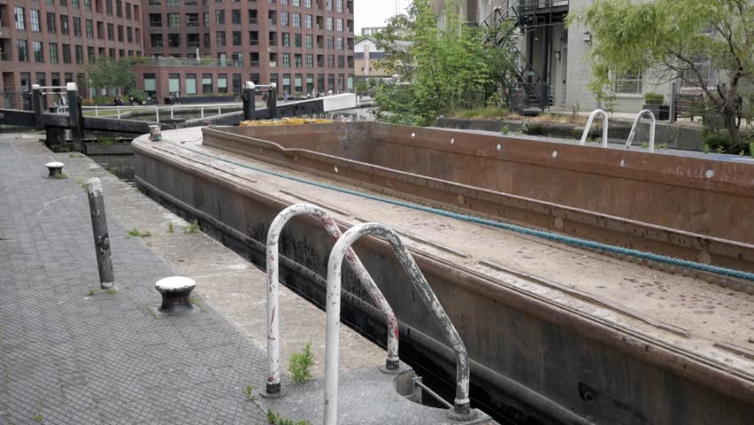 Commercial narrowboat transport for industry and construction activity. Material delivered along canal. Rope tighten and pulled to move boat out of lock chamber. Empty container on hopper. Push tug.