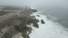 An aerial video of a rocky shore and a lighthouse with the sea waves on a cloudy day
