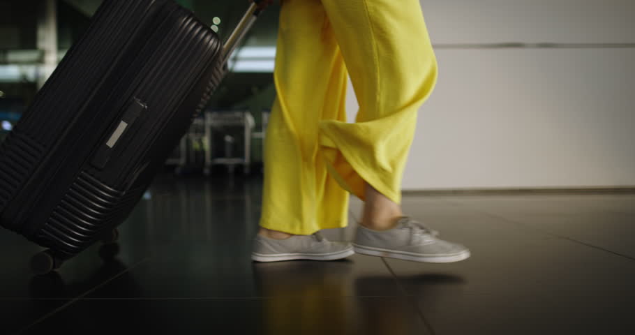 Legs of woman walk through airport. Woman traveler goes to waiting area to wait for her flight. Woman's legs and suitcase on wheels, which she rolls behind her. Passenger is walking through airport. Royalty-Free Stock Footage #1098600169