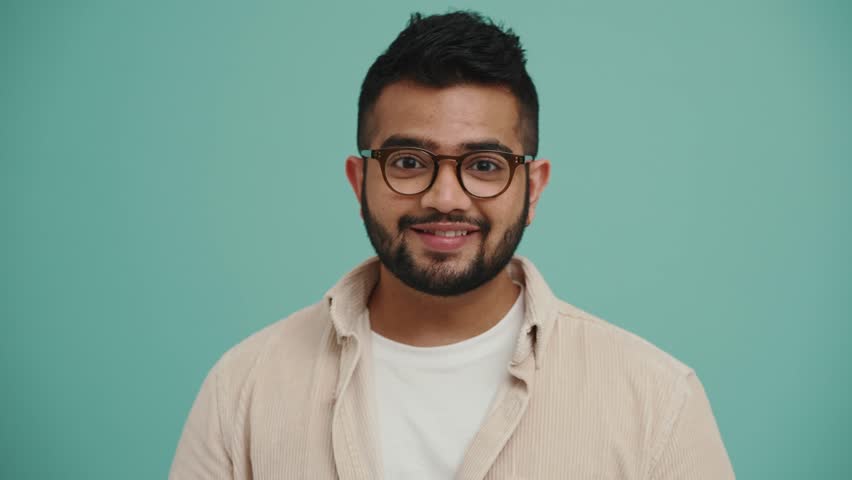 Happy Middle Eastern young man wearing eyeglasses waving hand at the camera in the turquoise studio | Shutterstock HD Video #1098600463