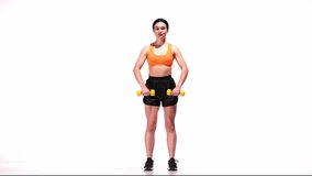Young sportive girl training with dumbbells over white studio background. Rising weights for strong hands. Modern sport, action, motion, youth concept. Fitness, hobby, healthy lifestyle