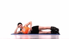 Young sportive girl training with legs weights over white studio background. Legs swings. Outer thigh lift. Modern sport, action, motion, youth concept. Fitness, hobby, healthy lifestyle