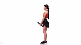 Young sportive girl training with sports equipment, weights over white studio background. Romanian thrust and squats. Modern sport, action, motion, youth concept. Fitness, hobby, healthy lifestyle