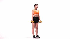 Full-body workout. Young sportive girl training with dumbbells over white studio background. Squats and hands exercises. Modern sport, action, motion, youth concept. Fitness, hobby, healthy lifestyle