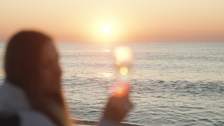Sunrise on the Sea, The girl admires the reflection of the sun's rays in a glass of Champagne. | Shutterstock HD Video #1098602199