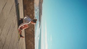 Yoga exercises with ocean view on background. Caucasian fit woman doing yoga training on seashore. Healthy lifestyle concept. Mid adult female practicing yoga and flexibility. Vertical video