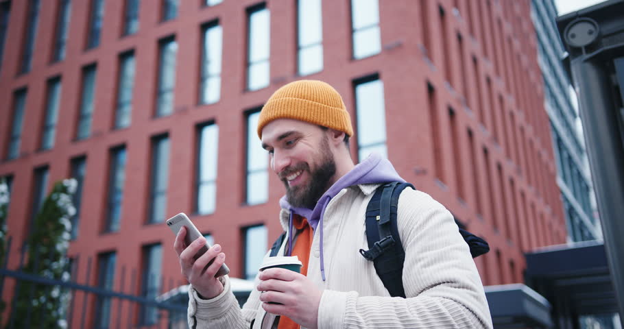 Portrait of adult handsome arab hipster man with beard wearing yellow hat using smartphone outdoors in the city streets at winter. Beautiful people, city lifestyle and urban youth culture concept. | Shutterstock HD Video #1098613177